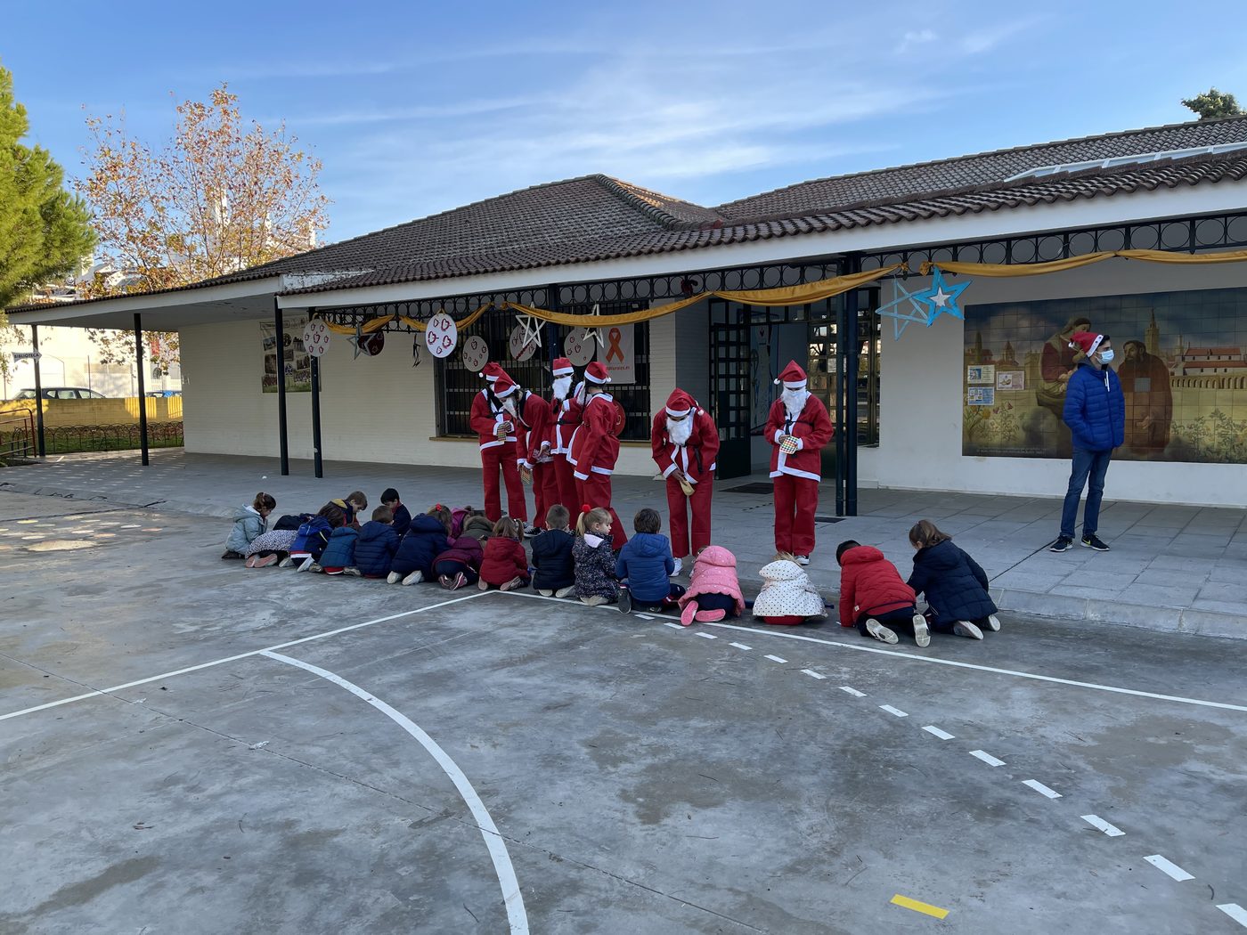Alumnos sentados y separados en el patio viendo una actuación navideña delante del porche