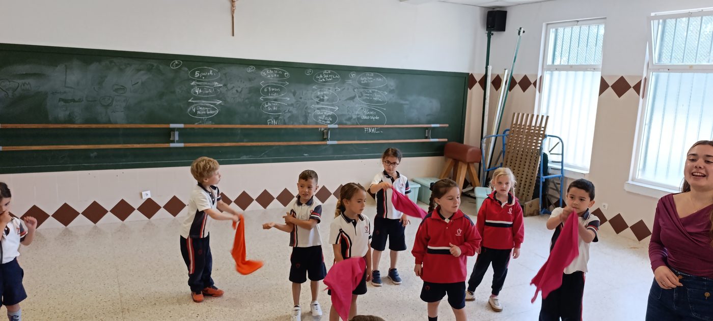 Niños de Infantil en corro en una sala diáfana, haciendo un juego de movimiento con su maestra