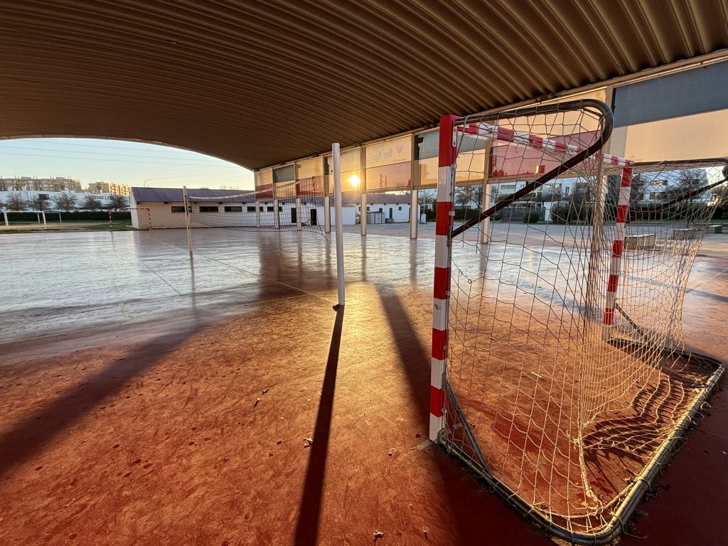 Pista cubierta de suelo rojo, con portería y red de voleibol, al atardecer