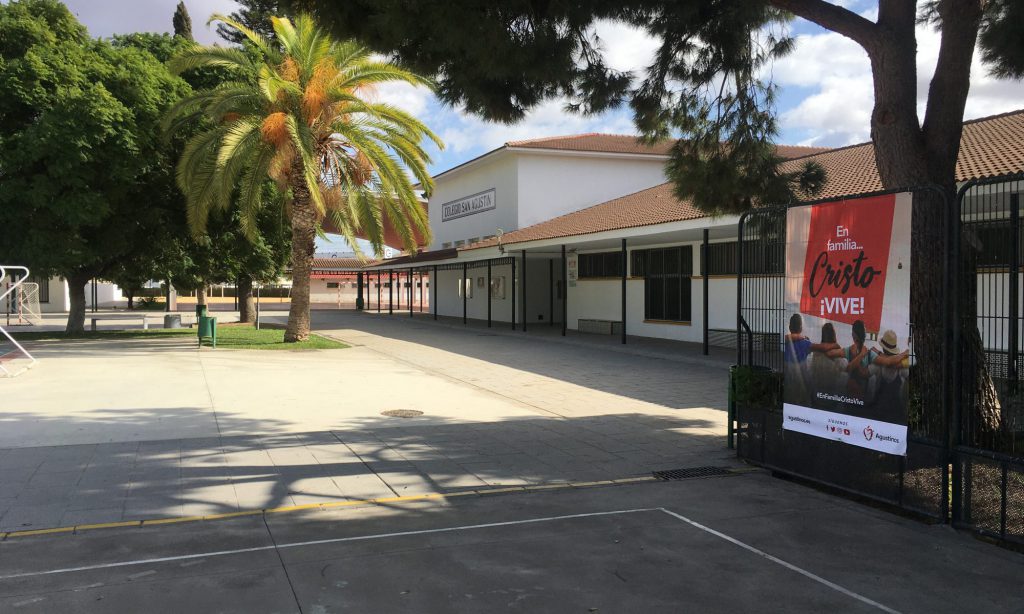 Patio principal del colegio, con palmeras y una pancarta granate en la valla