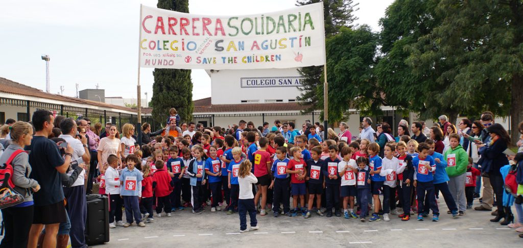 Cientos de alumnos reunidos en el patio bajo una pancarta que dice «Carrera solidaria»