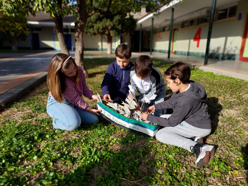 Cuatro alumnos montan juntos una maqueta sentados en el césped del patio