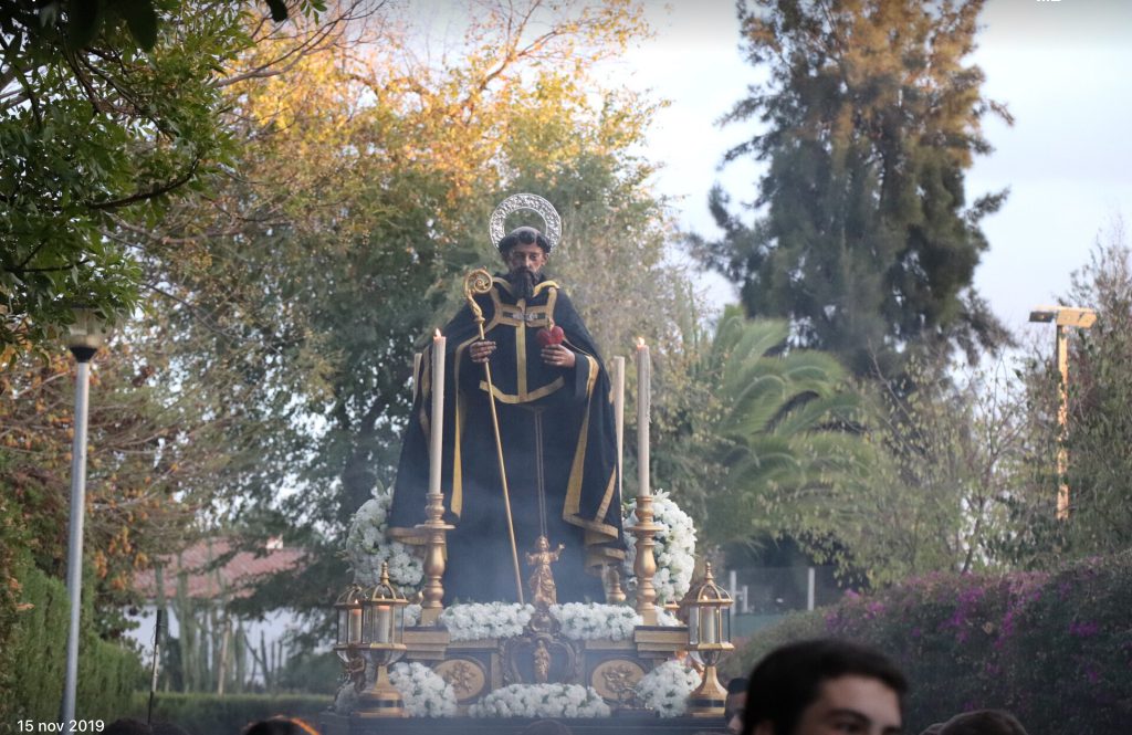 Paso procesional con la imagen de San Agustín, entre árboles y flores blancas, en el patio del colegio