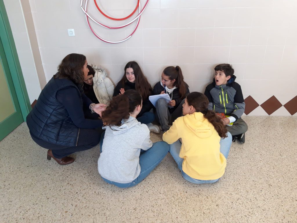Alumnos de Secundaria sentados en el suelo en corro con una profesora, conversando